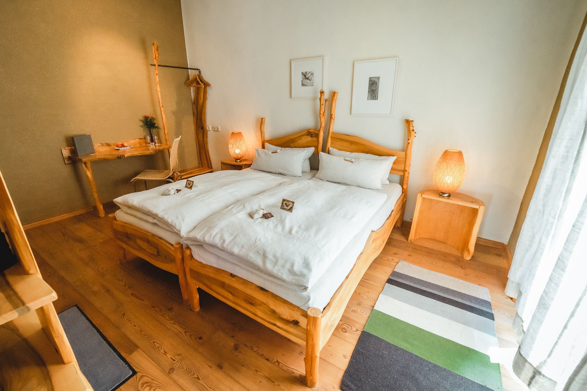 Ein gemütliches Schlafzimmer mit Holzmöbeln, einem Doppelbett, Nachttischen und einem Schreibtisch. Zwei Lampen und Bilder an der Wand ergänzen das Ambiente.