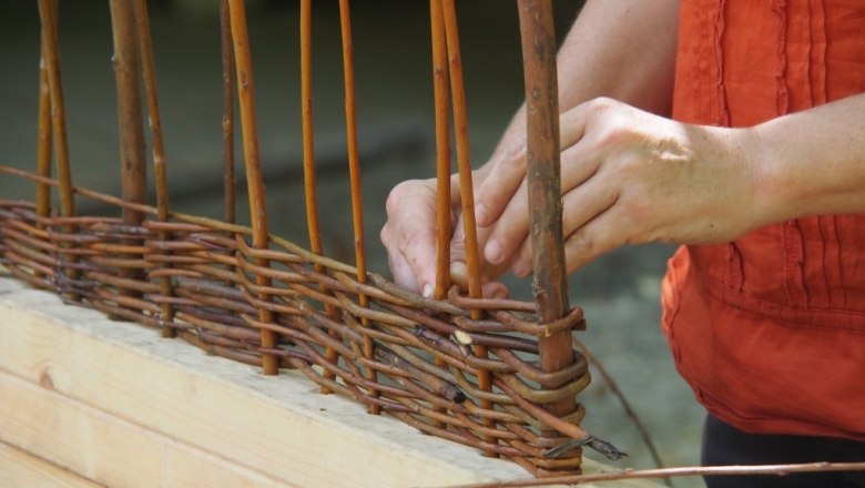 Person weaves willow branches into a basket.