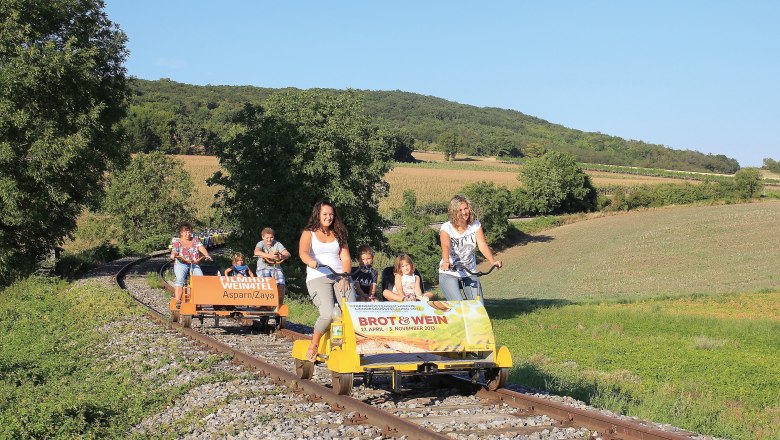 People ride on a trolley through a rural landscape.