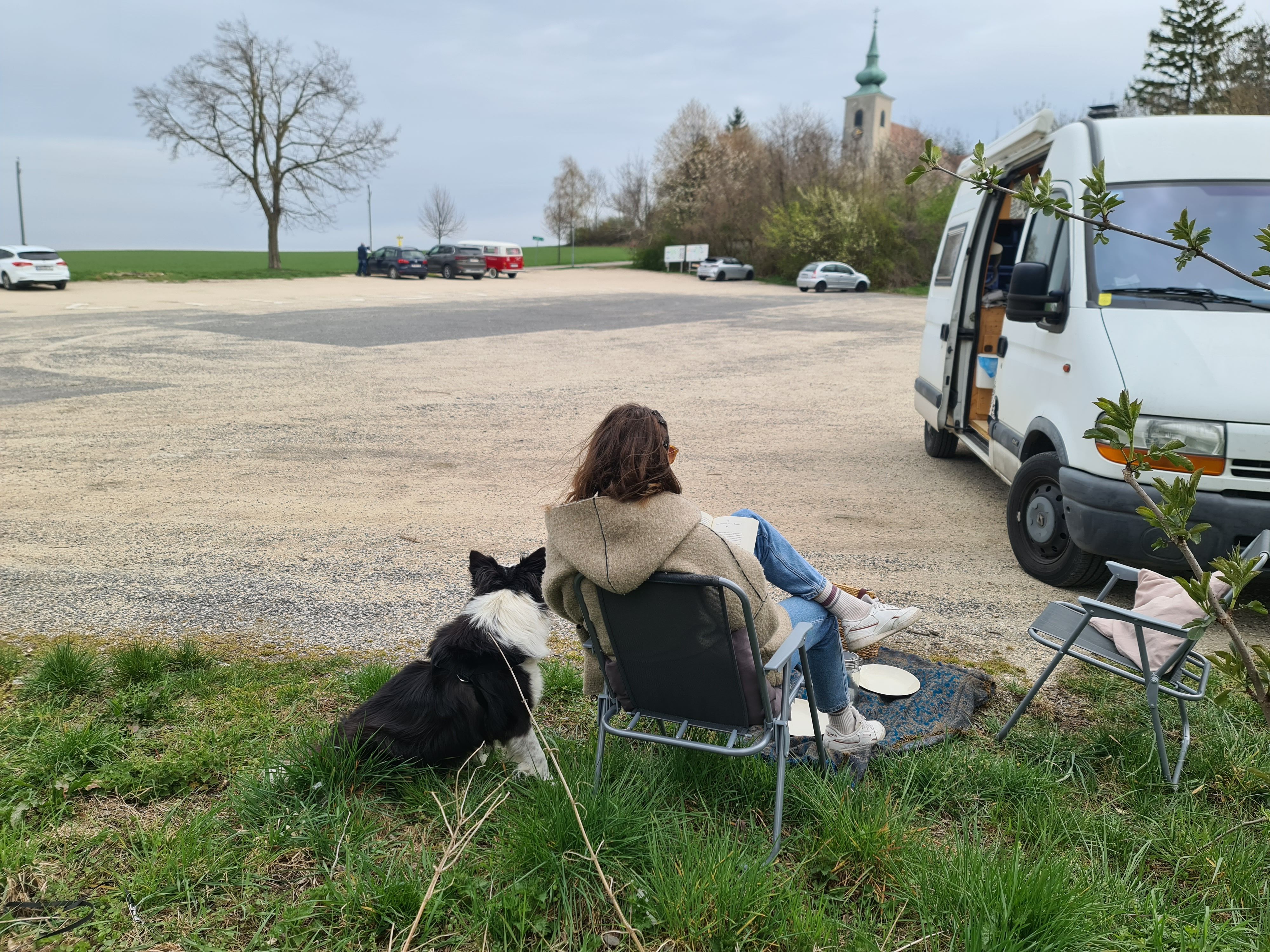 Dame mit Hund neben weißen Campingbus und Blick auf Oberleiserberg mitK Kirche